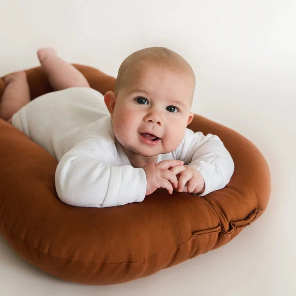 Adorable baby enjoying ultimate comfort on a premium gingerbread-colored cocoon bed. Designed to provide ergonomic support, breathable materials, and a safe, snug space for newborns and infants. Perfect for restful sleep, tummy time, and cozy moments with your little one